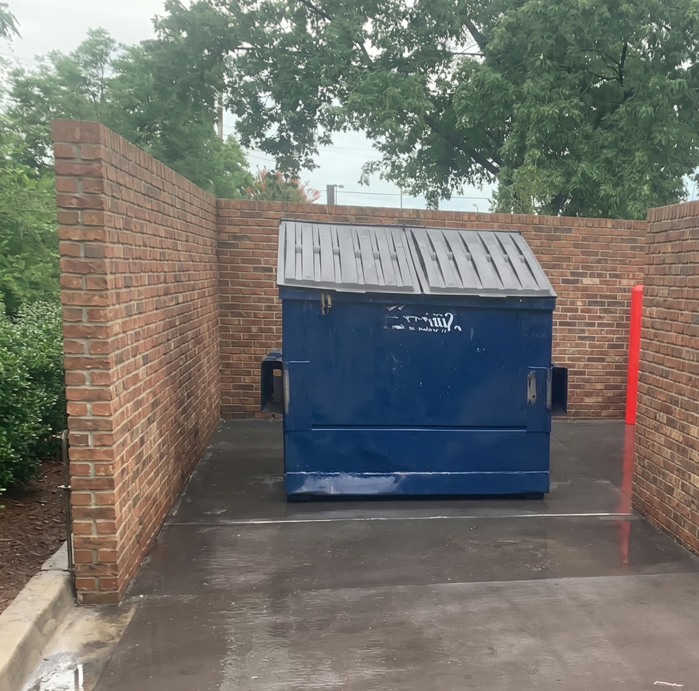 Freshly pressure-washed dumpster pad and brick enclosure
